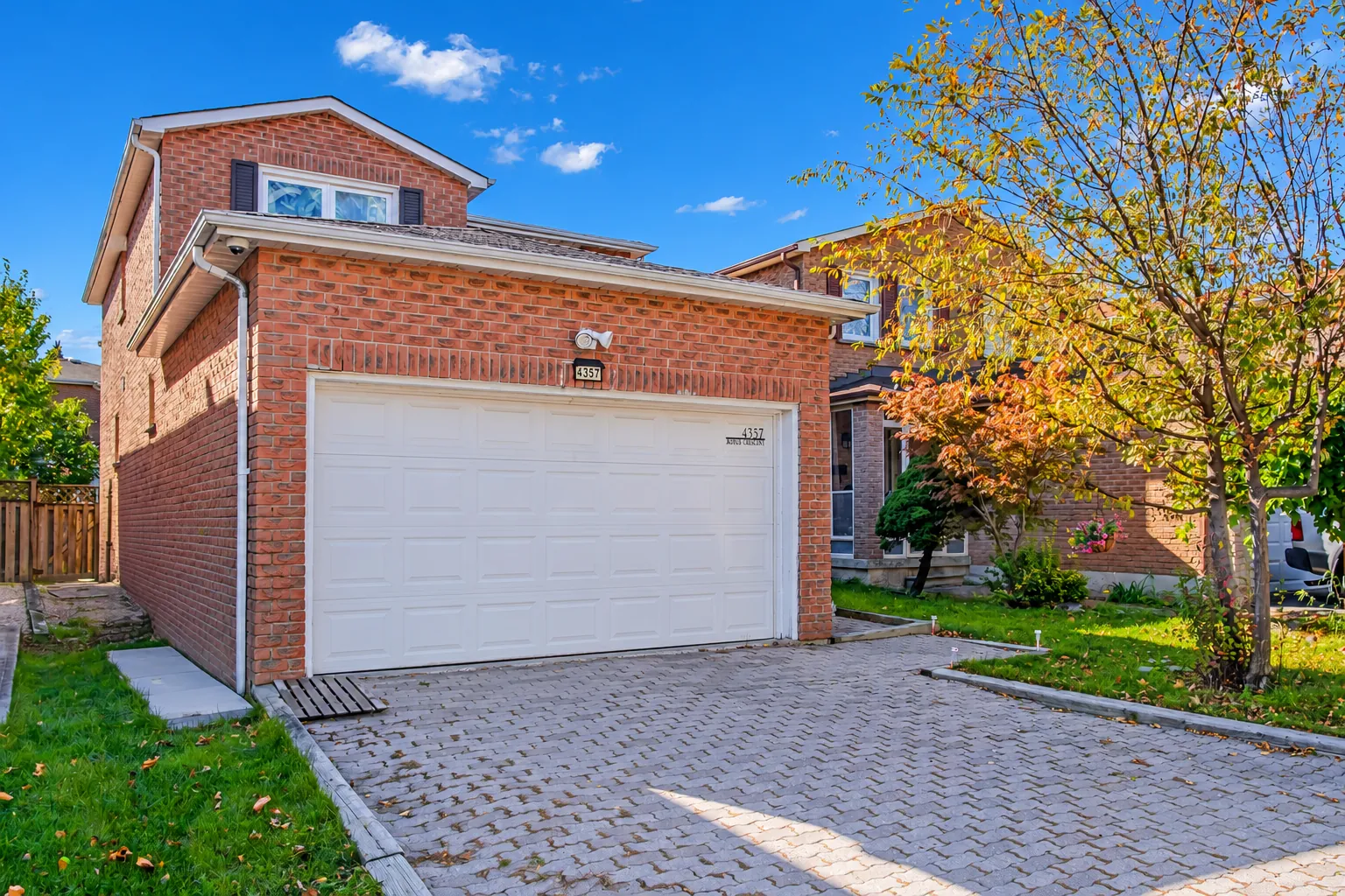 The front at an angle: the brick garage and the gable above it, a lawn beside the drive, a maple turning yellow