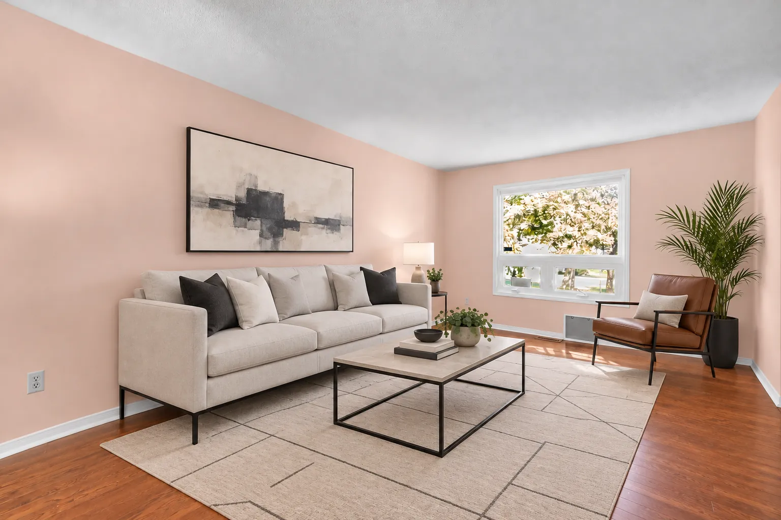 The living room virtually staged from the other side: a long pale sofa, a leather lounge chair, a coffee table, a palm, a large print over the sofa
