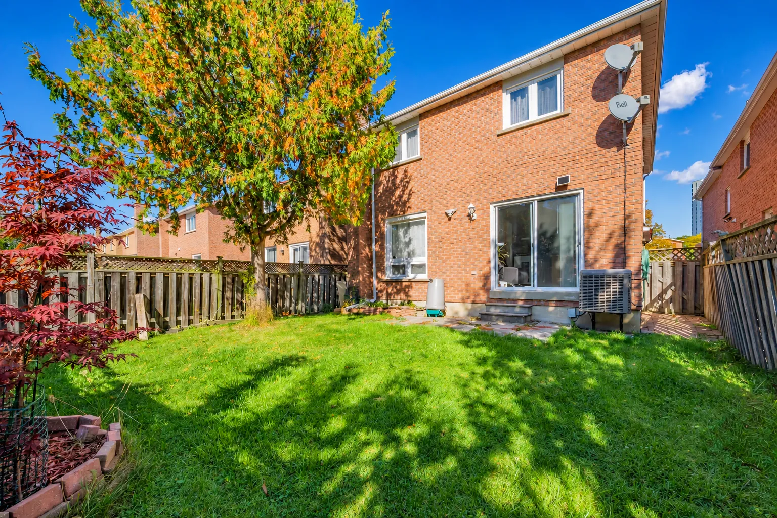 The back of the house: red brick, a sliding glass door at ground level, an air conditioner, a lawn and a maple, wood fences